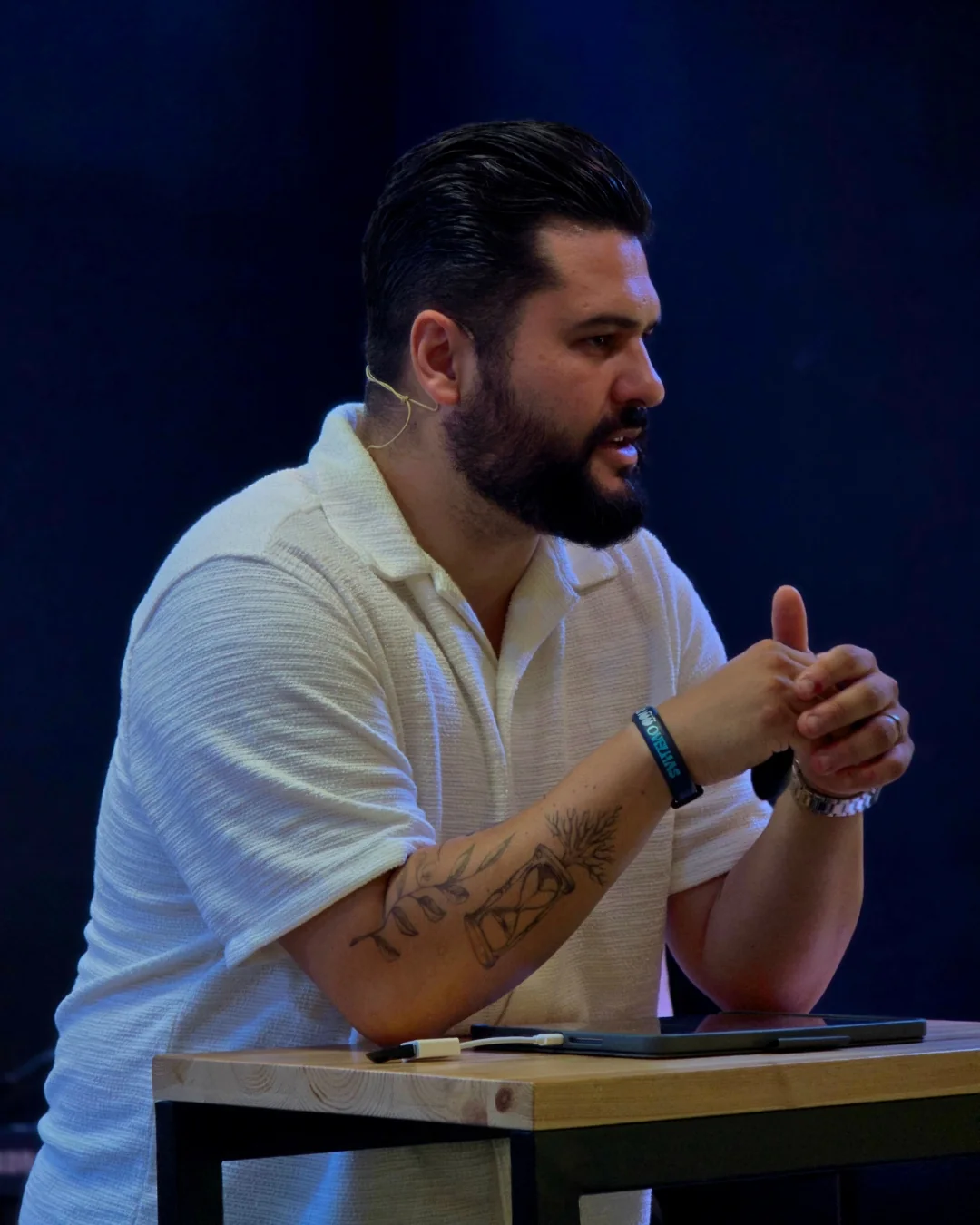 Il Pastore Thomas Abelini seduto sul palco, in camicia bianca, mentre parla alla chiesa