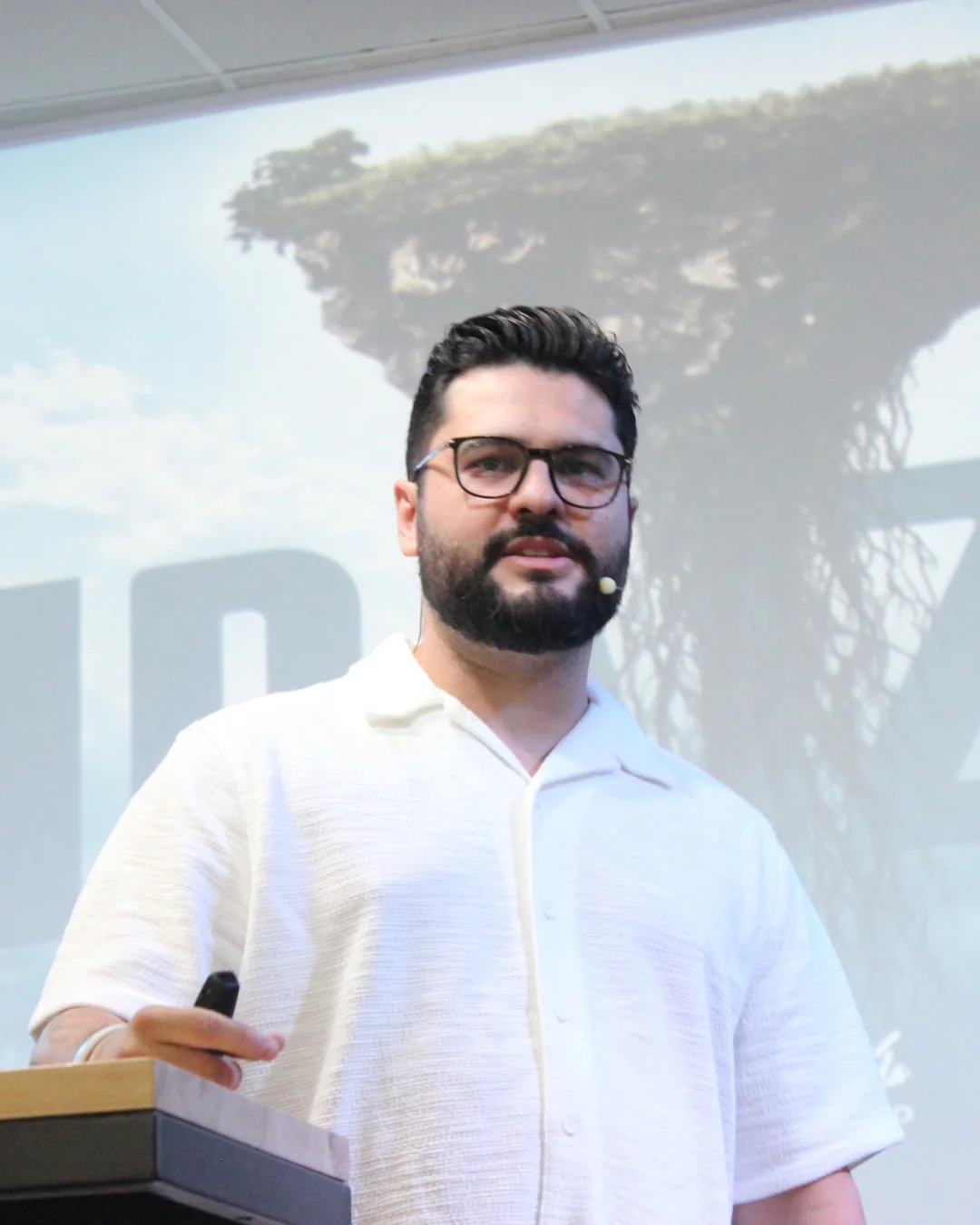 Il Pastore Thomas Abelini in camicia bianca mentre predica davanti a uno schermo chiaro